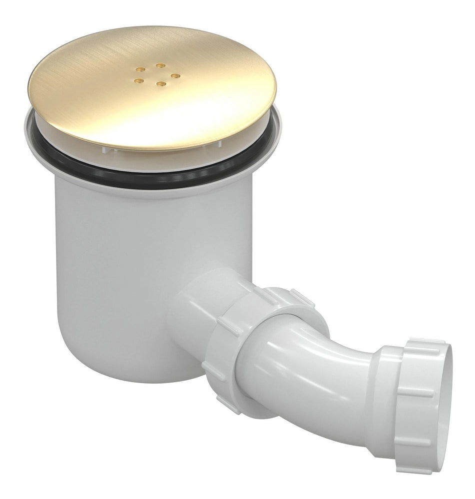 Brushed brass low-profile waste cover on white drain body with outlet pipe.